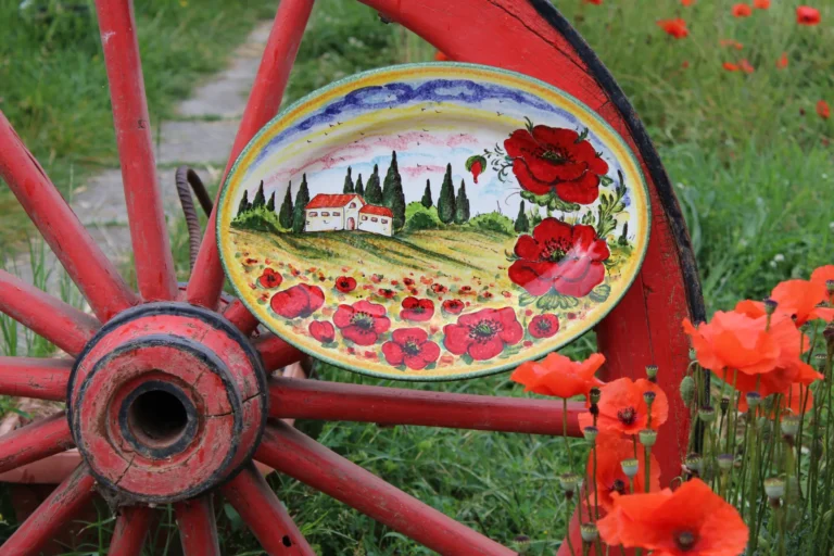 On a green summer field with red poppies there is a beautiful handpainted tray showing the same tuscan landscape with a white farm and may red poppies.